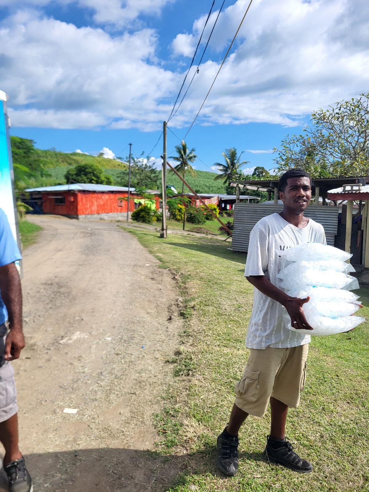A customer carrying a stack of Bula Ice bags in a village